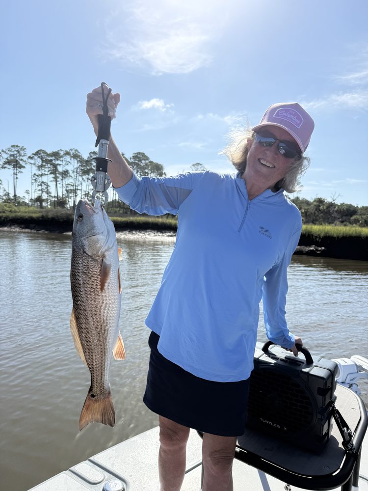 Angler lifting a redfish on a fish grip in a marsh creek