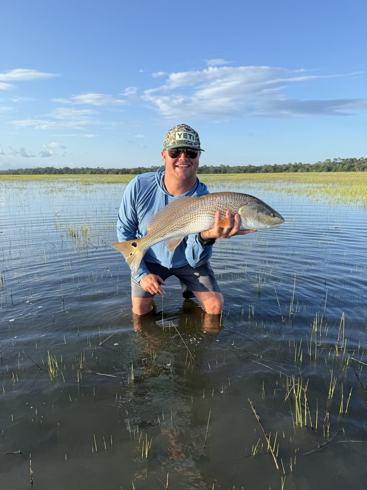 Angler kneeling on a flooded grass flat with a redfish