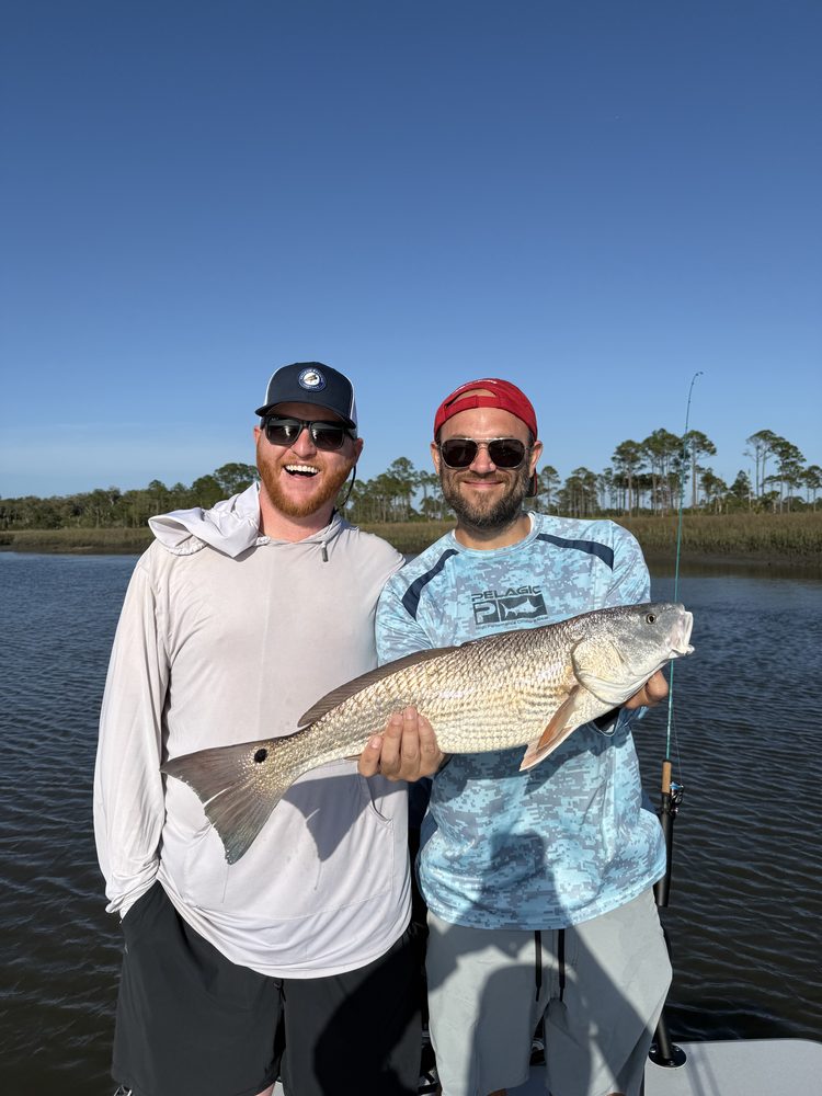 Two friends holding a redfish on the skiff
