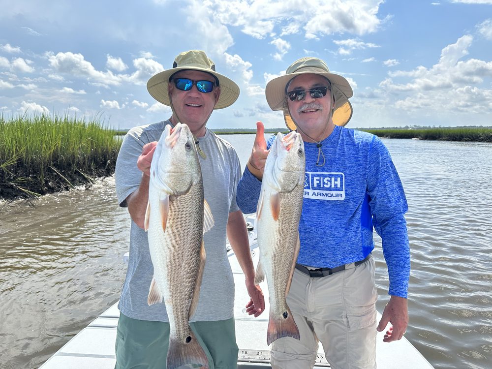 Two anglers in the marsh holding redfish