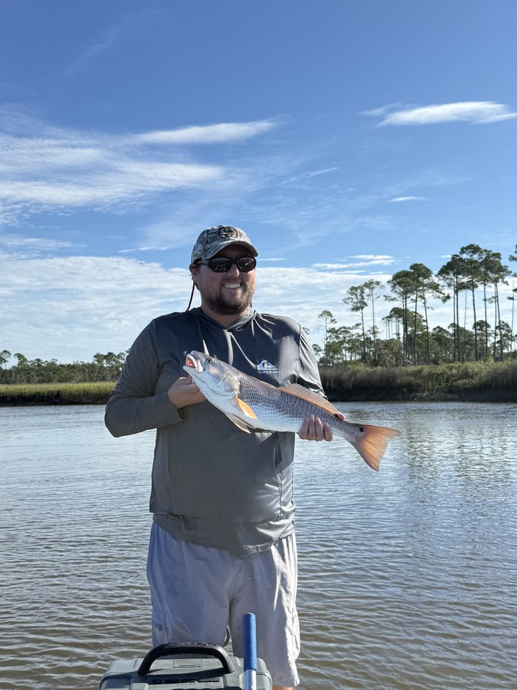 Angler holding a redfish with pine trees behind