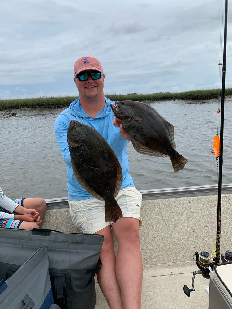 Angler on the skiff holding two flounder