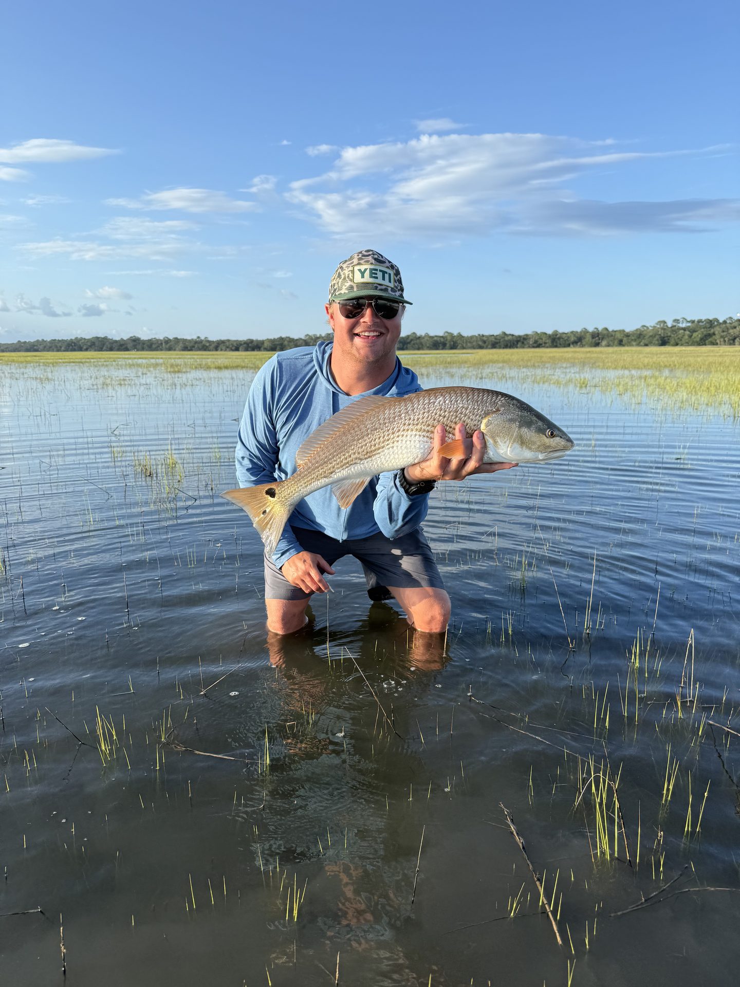 Angler kneeling on a flooded grass flat holding a large redfish