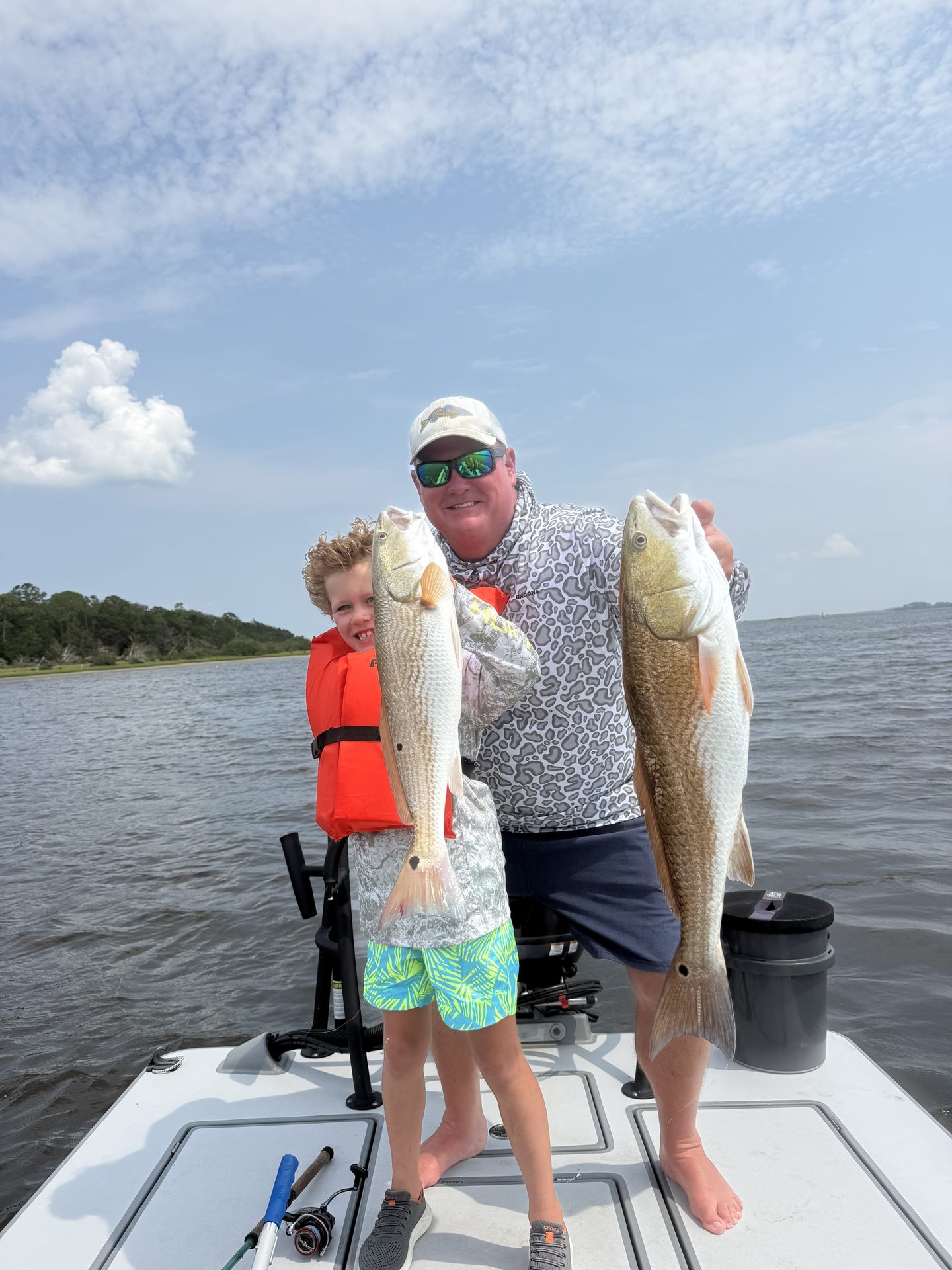 A father and his young son each holding a redfish on the bow of the skiff