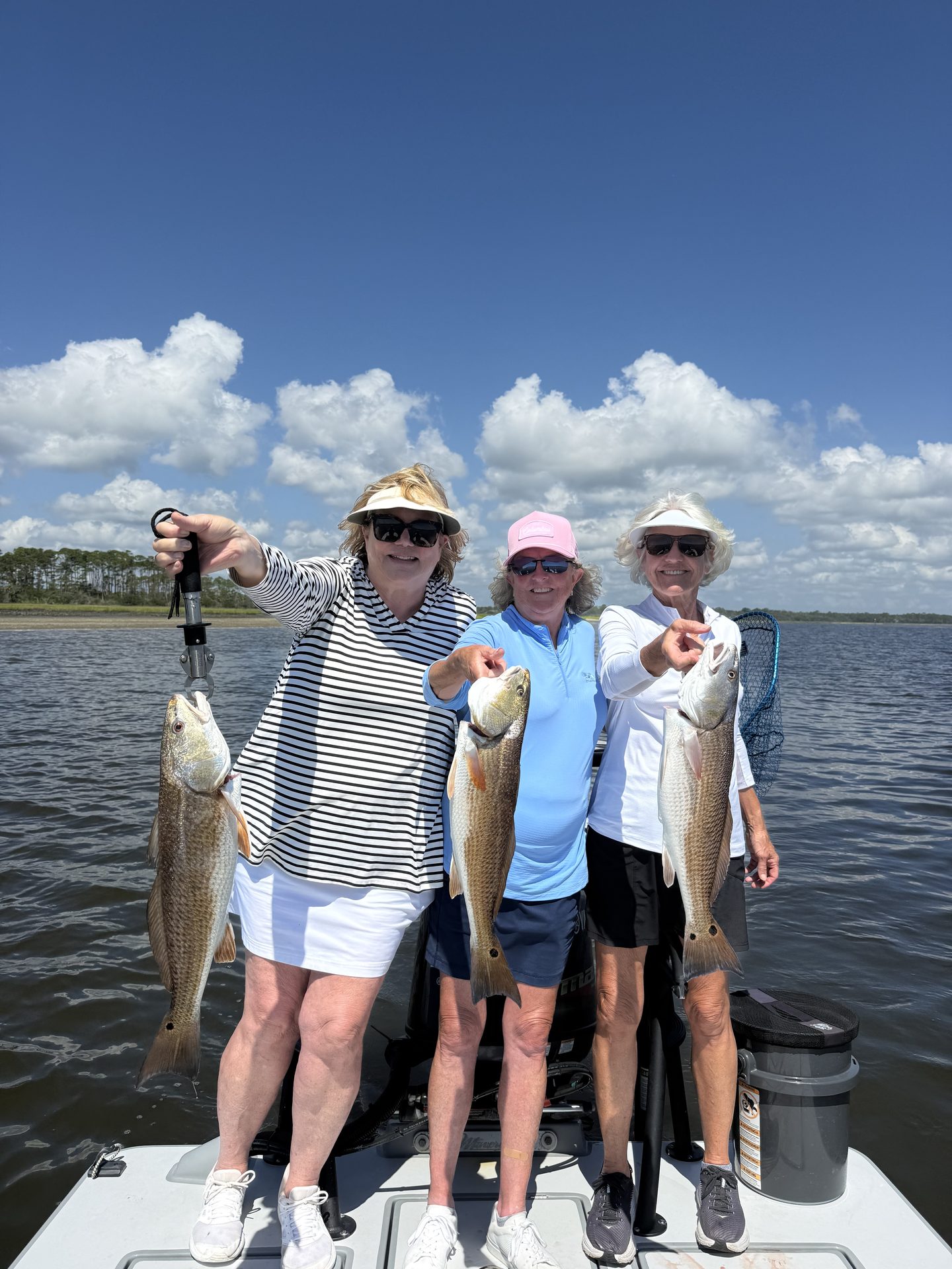 Three anglers on the bow each holding a redfish